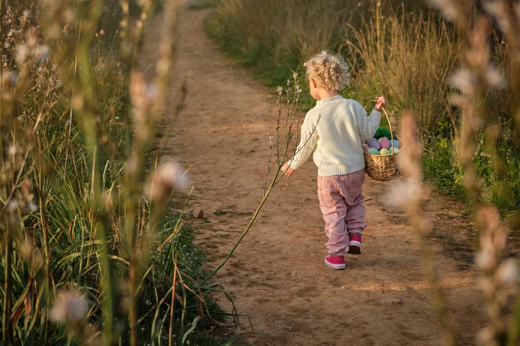 Cute little girl carrying basket with Easter eggs in countryside